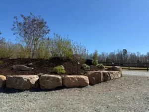 Boulder retaining wall being installed on a sloped yard to stabilize soil and prevent erosion.
